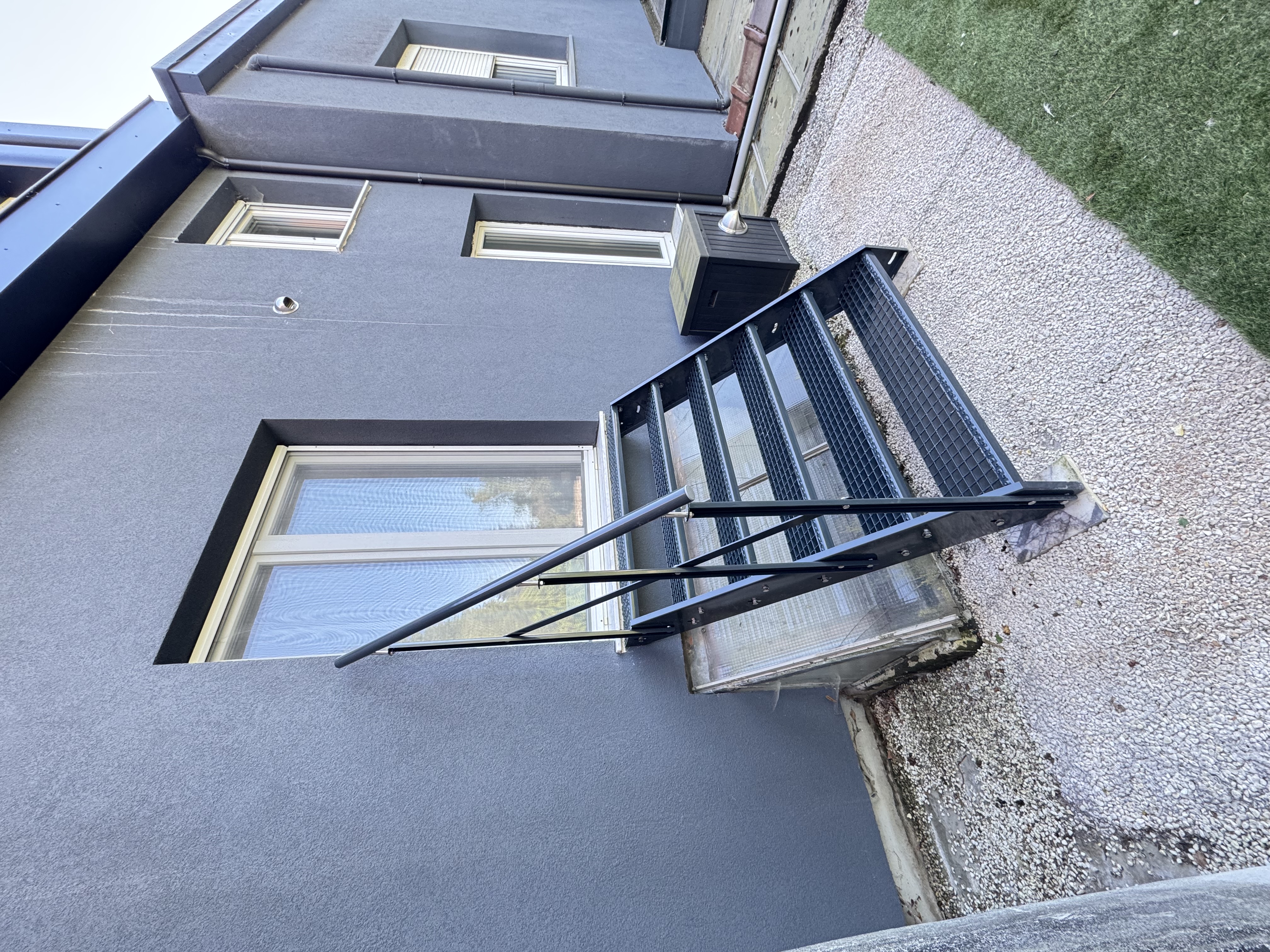 Black powder-coated steel external escape ladder, fixed to the rear facade.